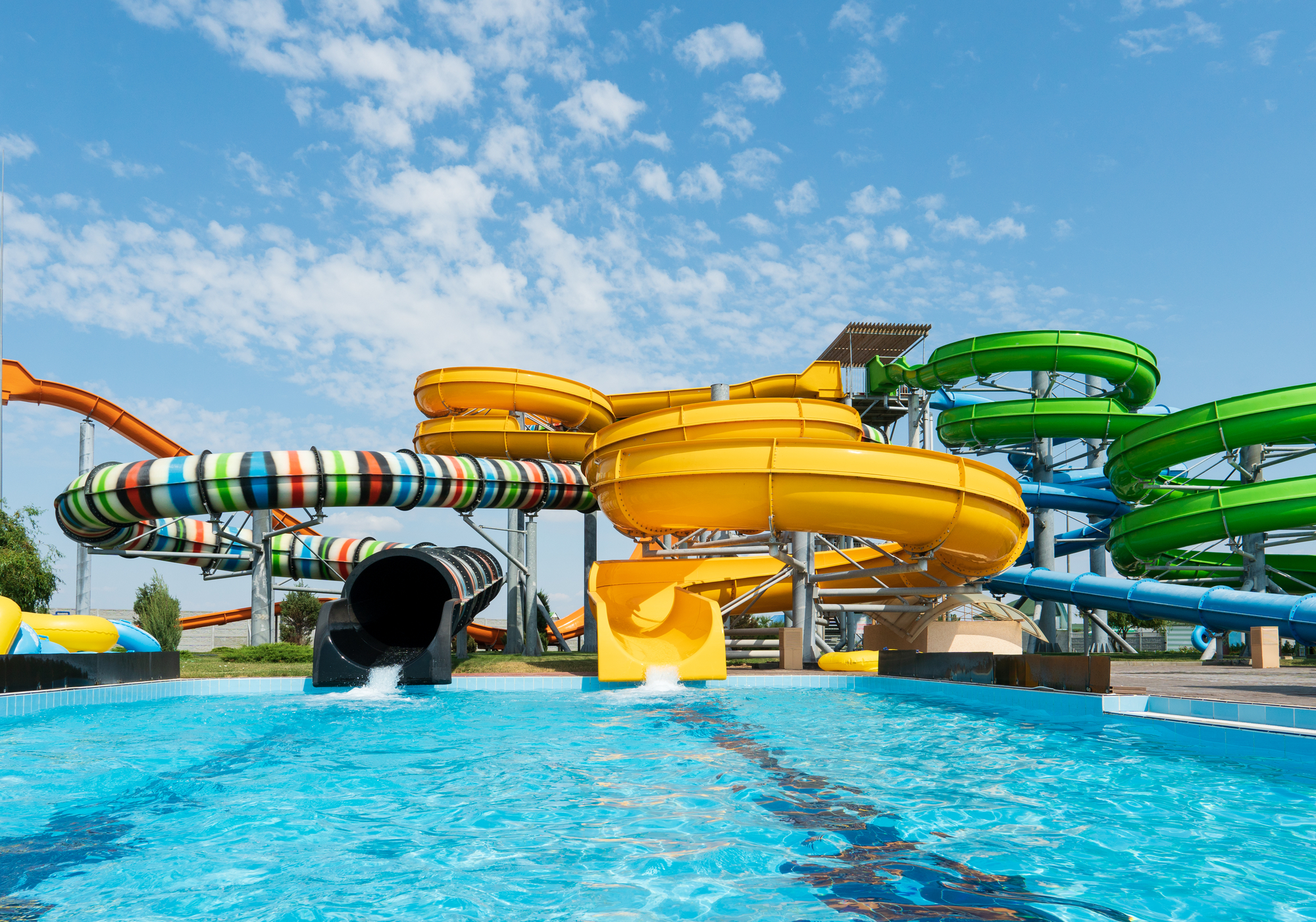 Water park, bright multi-colored slides with a pool. A water park without people on a summer day with a beautiful, cloudy blue sky.